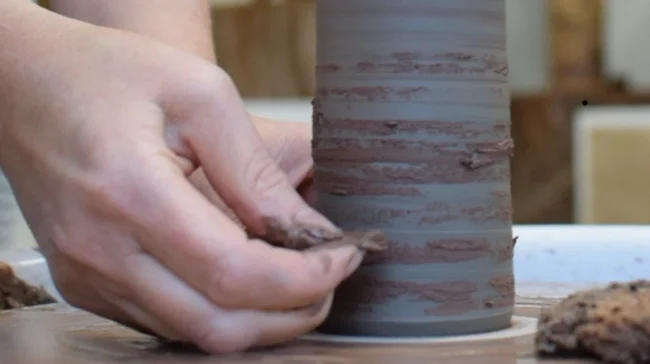 Hands sweeping wild clay slip onto a clay cylinder in Sonya Wilkins pottery studio using quiet presence to connect with earth material