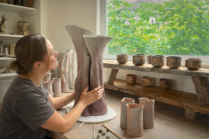 Sonya Wilkins touching a newly made ceramic tree vessel in raw clay, in her studio, showing intimate connection to clay as her making medium