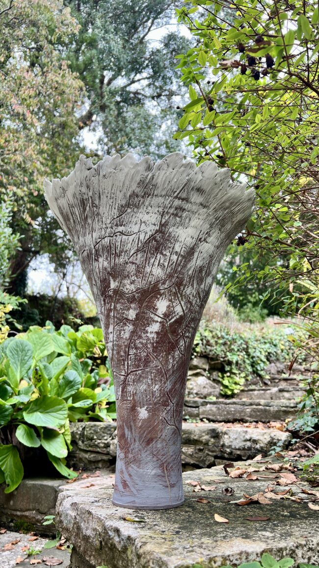 Clay vessel inspired by a Cotton Poplar Tree by Sonya Wilkins Ceramics sat on a stone wall in a garden setting with green foliage in the background