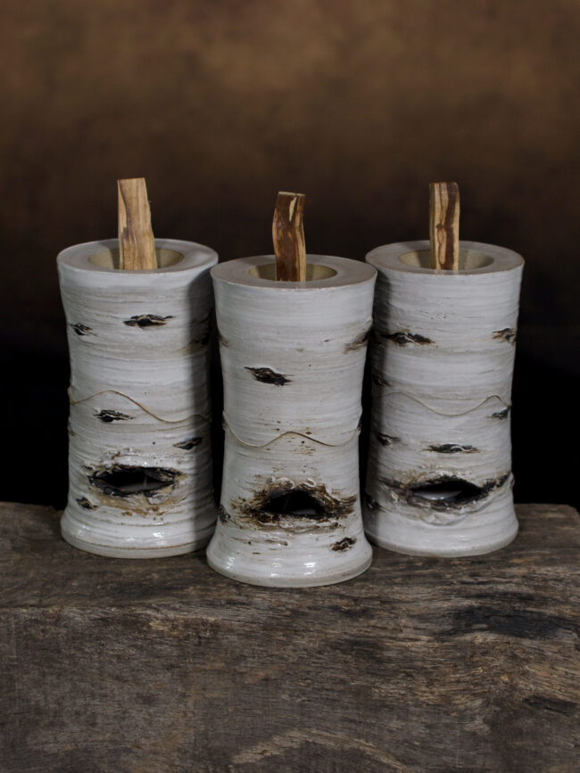Three white ceramic wood burners for palo santo wood. Inspired by the colour of silver birch trees with convection holes as lenticels of the tree so a candle can be placed inside to smoulder the wood placed inside the ceramic tube above.